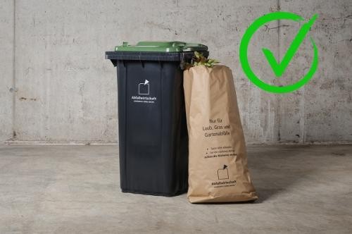 Biotonne mit einem gefüllten Laubsack daneben und ein grüner Haken