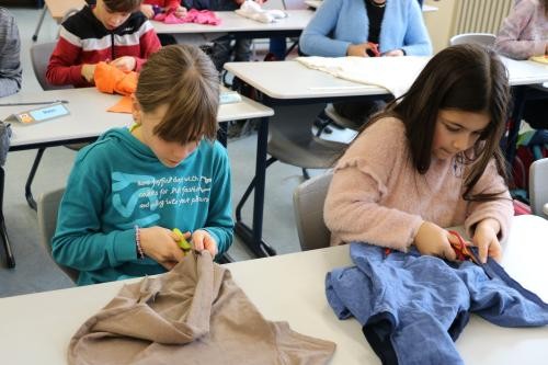 Zwei Kinder schneiden mit der Schere ein T-Shirt in Streifen
