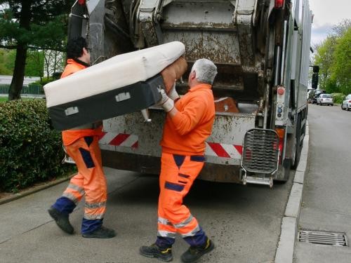 Zwei Mitarbeiter der Sperrmüllabholung verladen ein altes Sofa in das Presswerk des Sammelfahrzeuges