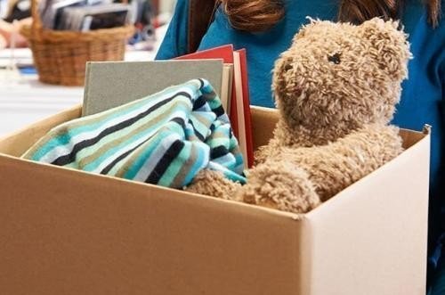 Karton mit Büchern, Teddybär und Kuscheldecke