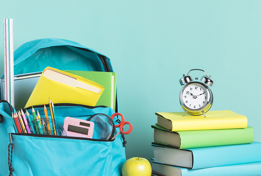 Bücher neben Schulranzen mit Heften, Stiften und weiteren Schulmaterialien